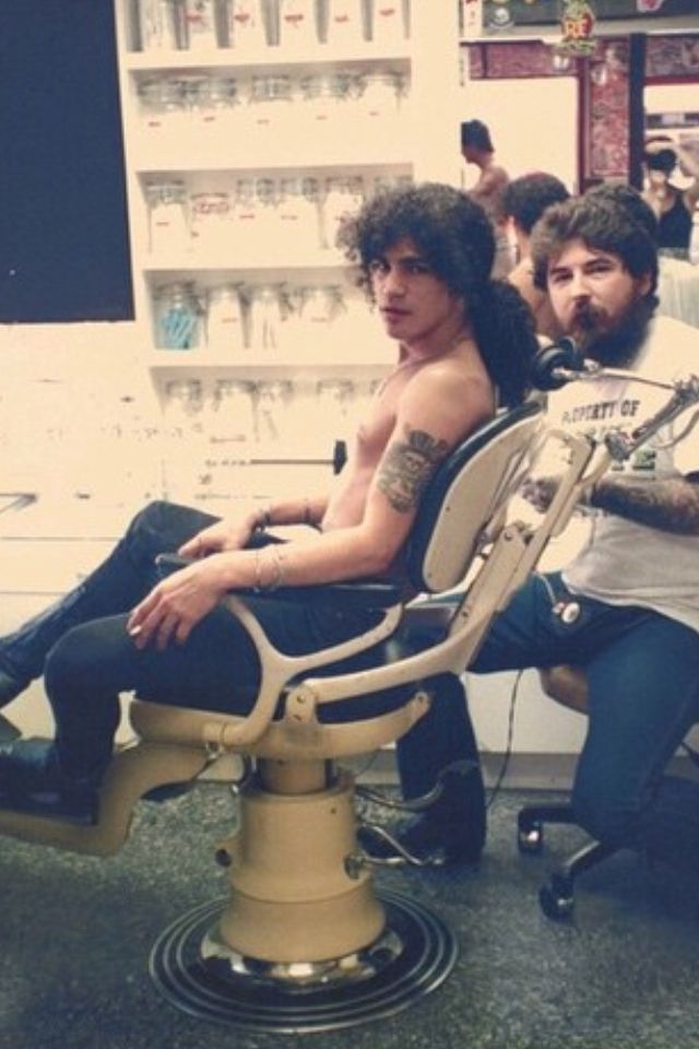 two men sitting in an office chair with their feet on the barber's chair