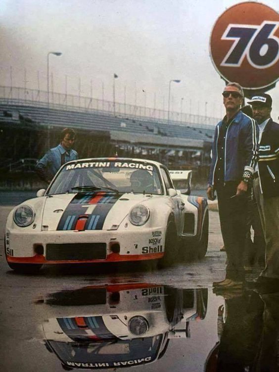 two men standing next to each other in front of a race car with the number 76 on it