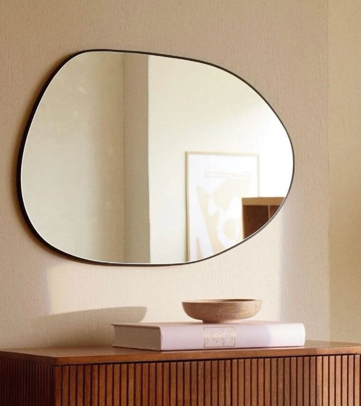 a round mirror on the wall above a wooden dresser with a bowl and book in front of it