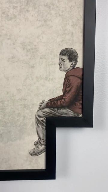 two framed pictures hang on the wall next to each other, one with a drawing of a boy sitting down