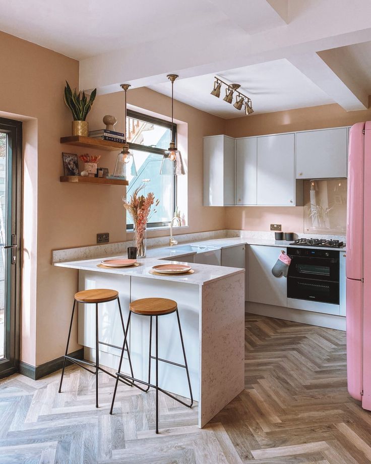 a kitchen with two stools in front of the island and pink refrigerator freezer