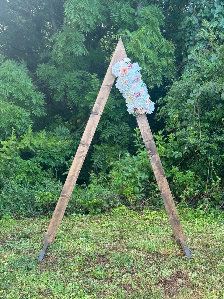 a wooden sign sitting on top of a grass covered field next to trees and bushes