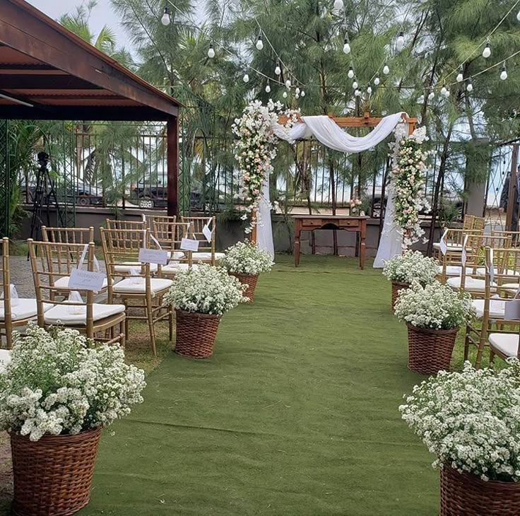 an outdoor wedding setup with white flowers and greenery on the grass, surrounded by wicker chairs