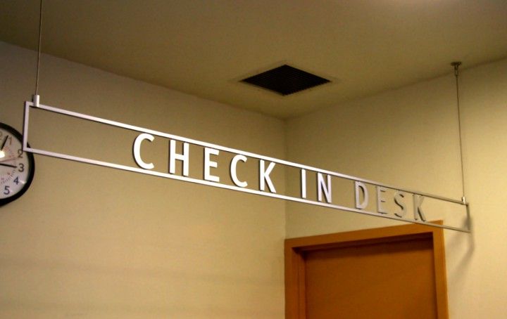 a clock hanging from the side of a wall next to a sign that reads check in desk