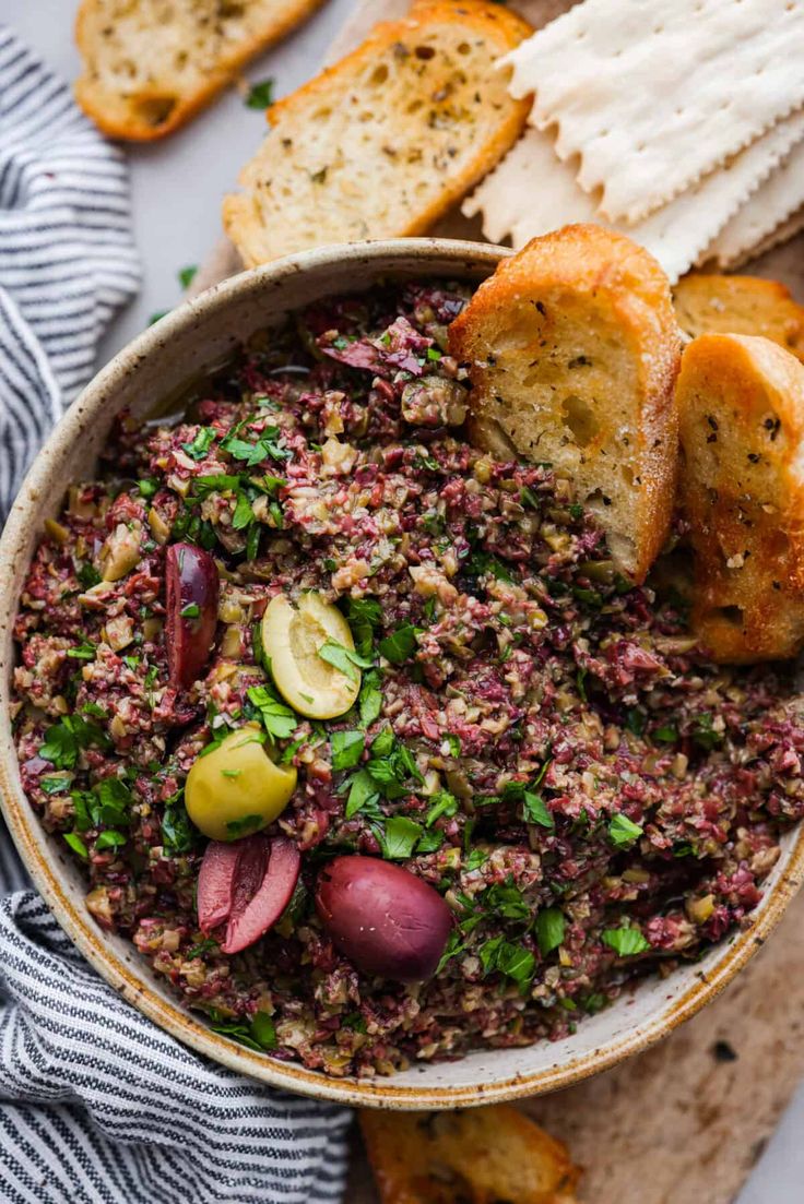 a bowl filled with food next to bread and crackers on top of a table