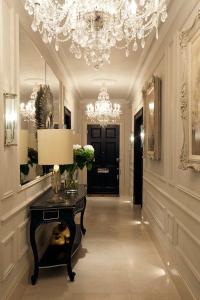 an elegant hallway with chandelier, mirror and vases on the side table