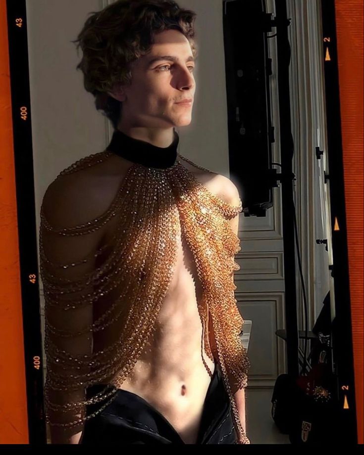 a young man with no shirt wearing chains on his chest and back, standing in front of a mirror