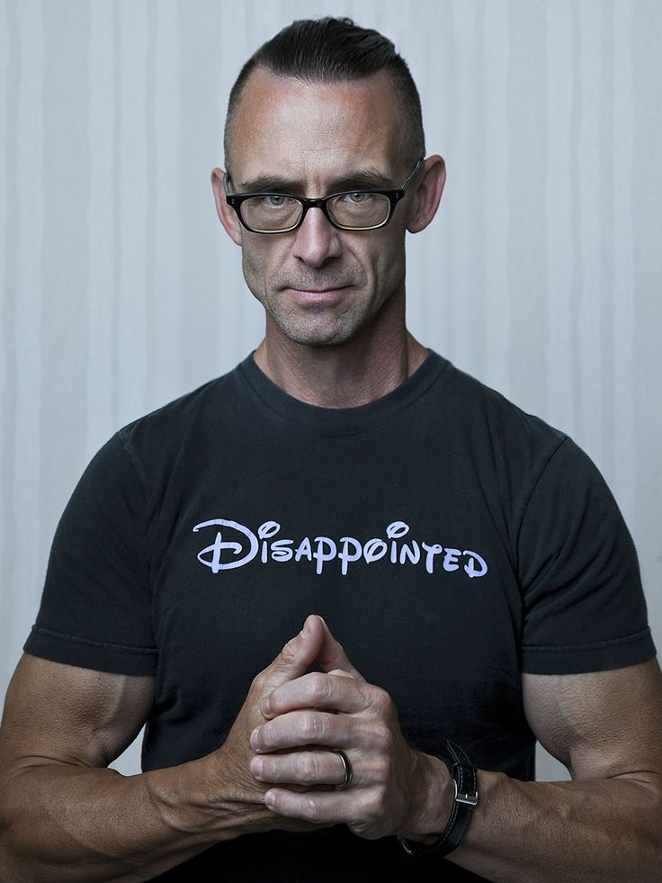 a man with glasses and a black shirt is looking at the camera while holding his hands together