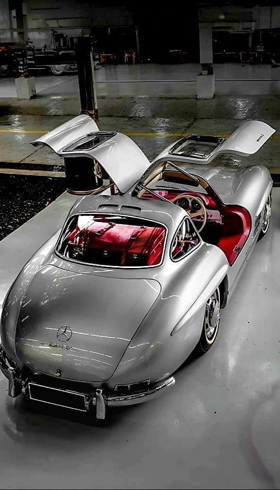 an old silver car parked in a garage with its hood up and the door open