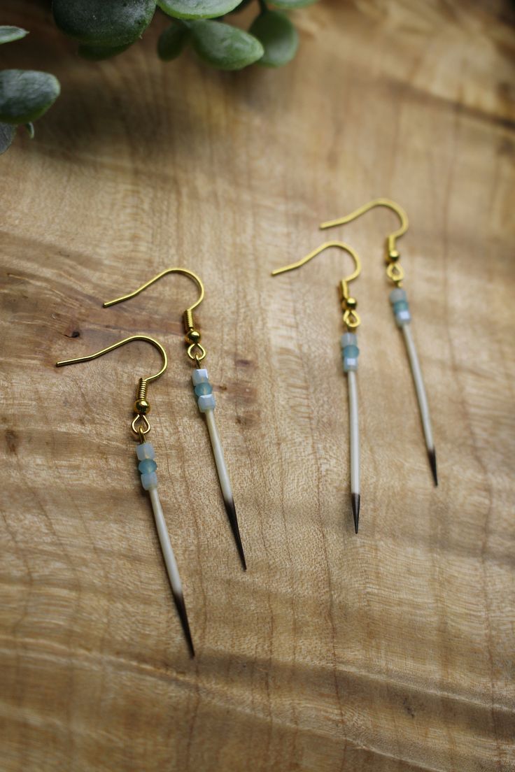 three pairs of earrings sitting on top of a wooden table next to a potted plant