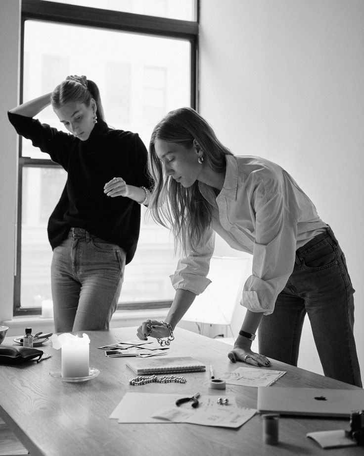 two women standing around a table with papers on it