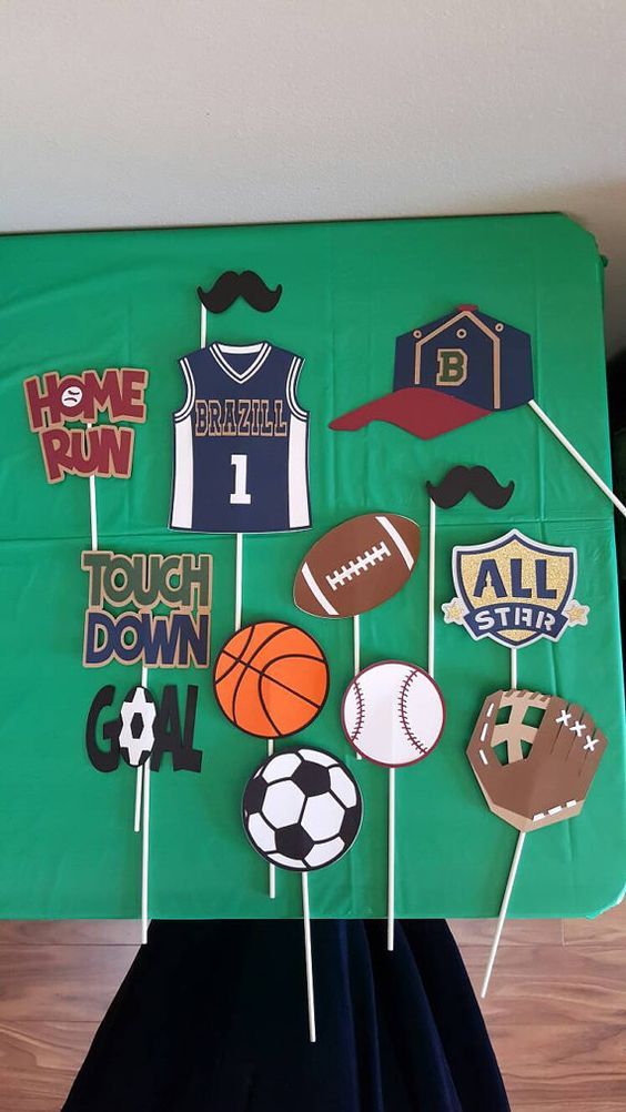 a green table topped with lots of cupcakes and cake toppers covered in sports related items