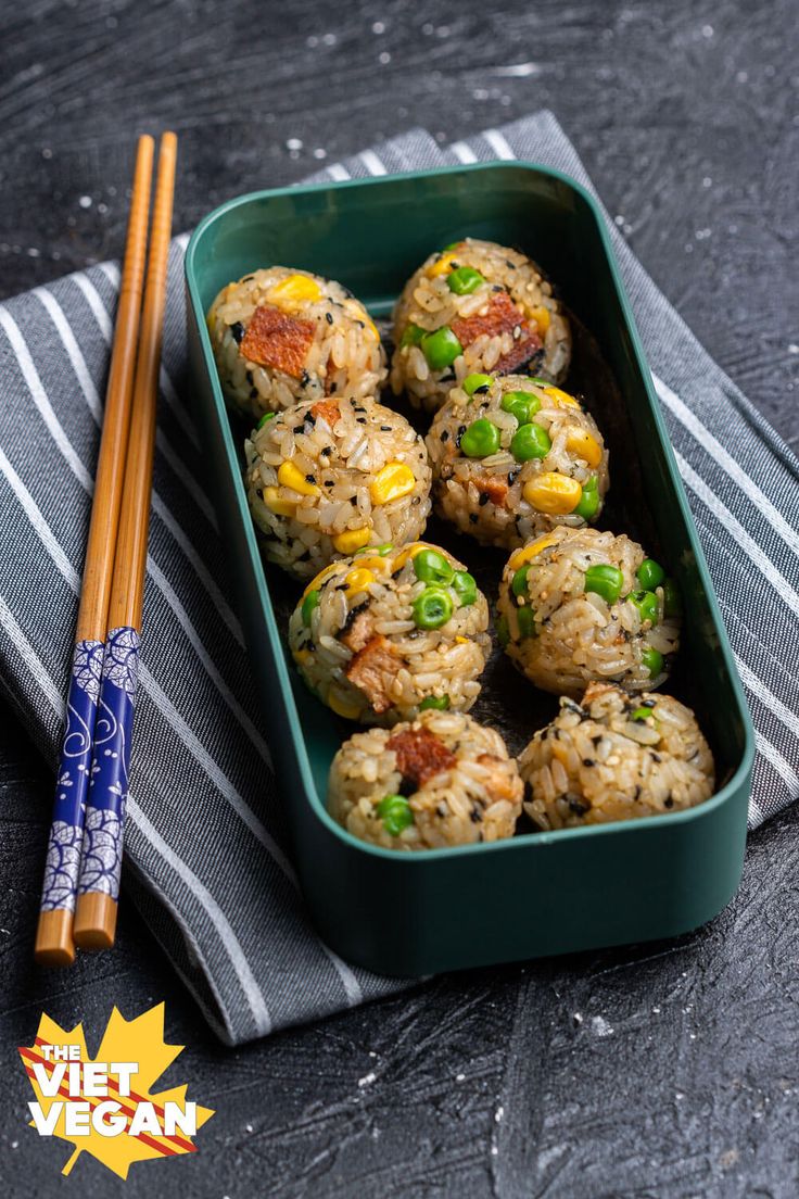 some food in a green container with chopsticks next to it