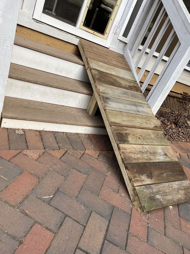 a wooden ramp sitting on top of a brick walkway next to a white door and window