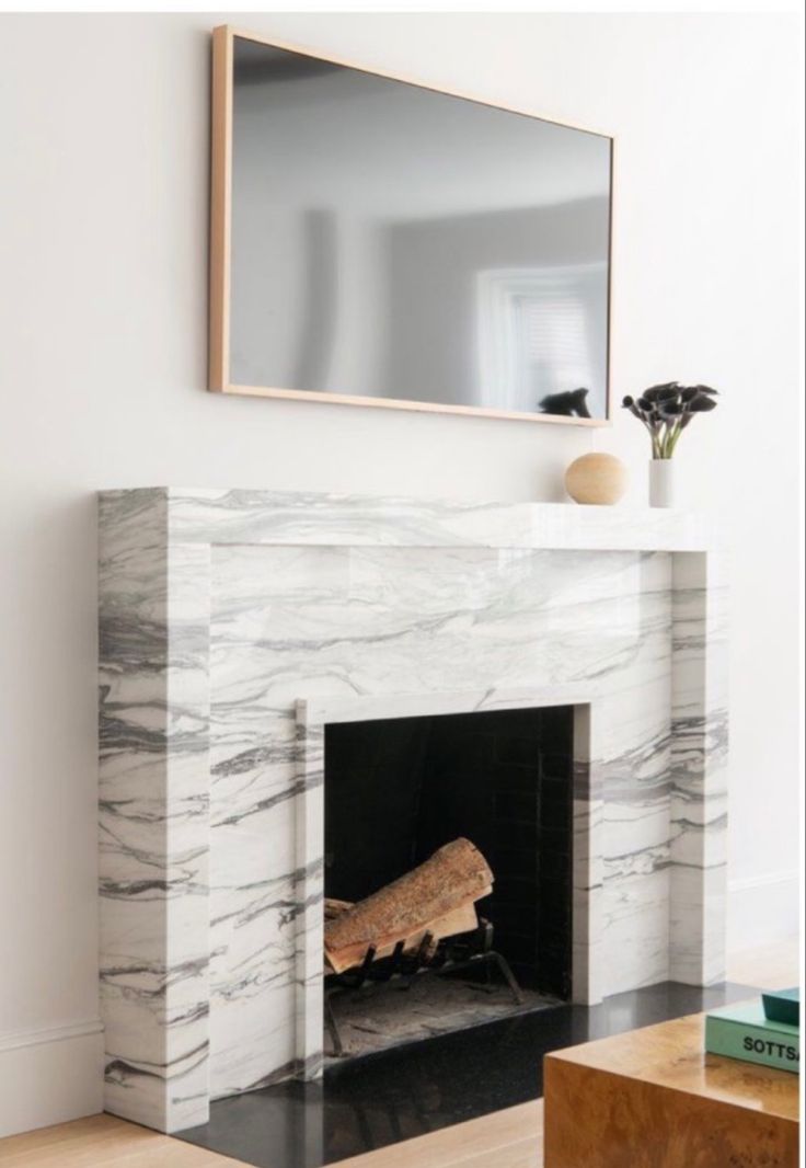 a fireplace with a mirror above it and some books on the table next to it