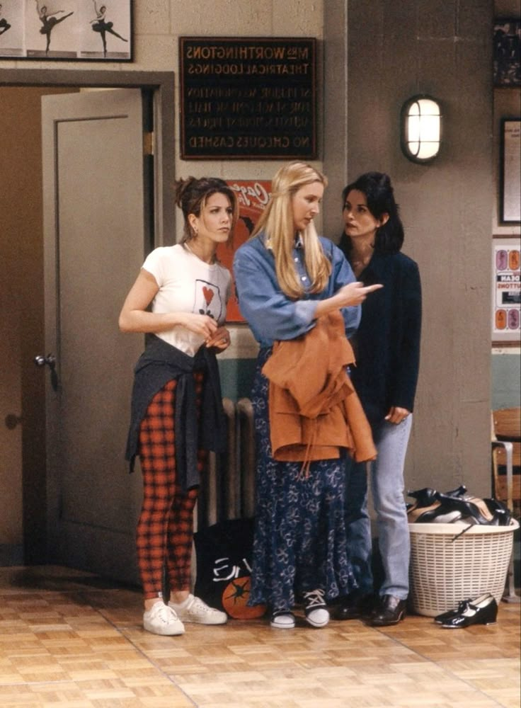 three women standing in front of a door talking to each other while one woman holds her hand out