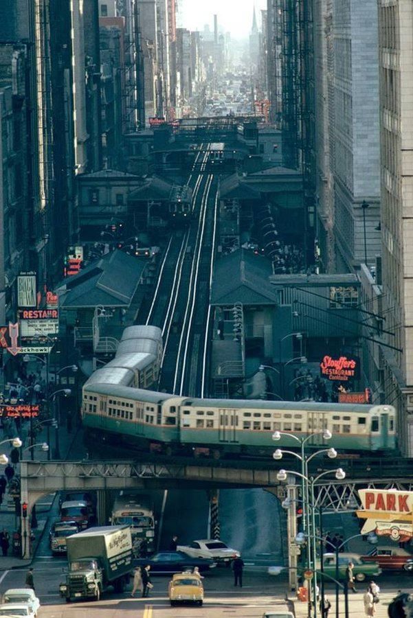 an overhead view of a train on tracks in the middle of city with tall buildings