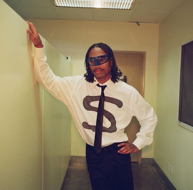 a man wearing sunglasses and a tie is standing in an office hallway with his hands on the wall