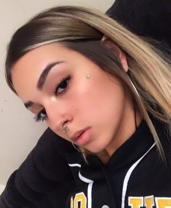 a woman with piercings on her nose and wearing a black hoodie is taking a selfie