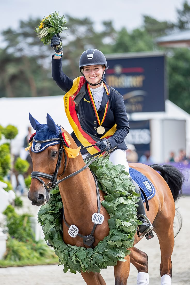 a woman riding on the back of a brown horse with a wreath around her neck