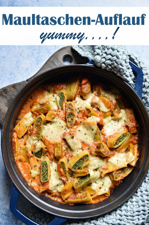 a skillet filled with pasta and sauce on top of a blue cloth next to a wooden spoon