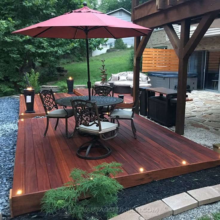 a deck with chairs and an umbrella is lit up by string lights on the patio