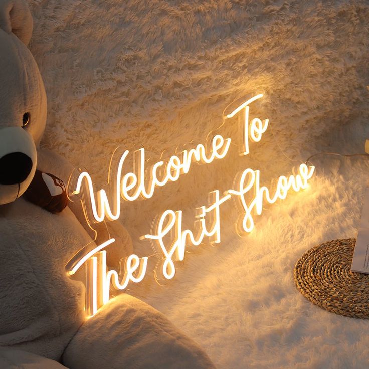 a white teddy bear sitting on top of a bed next to a light up sign