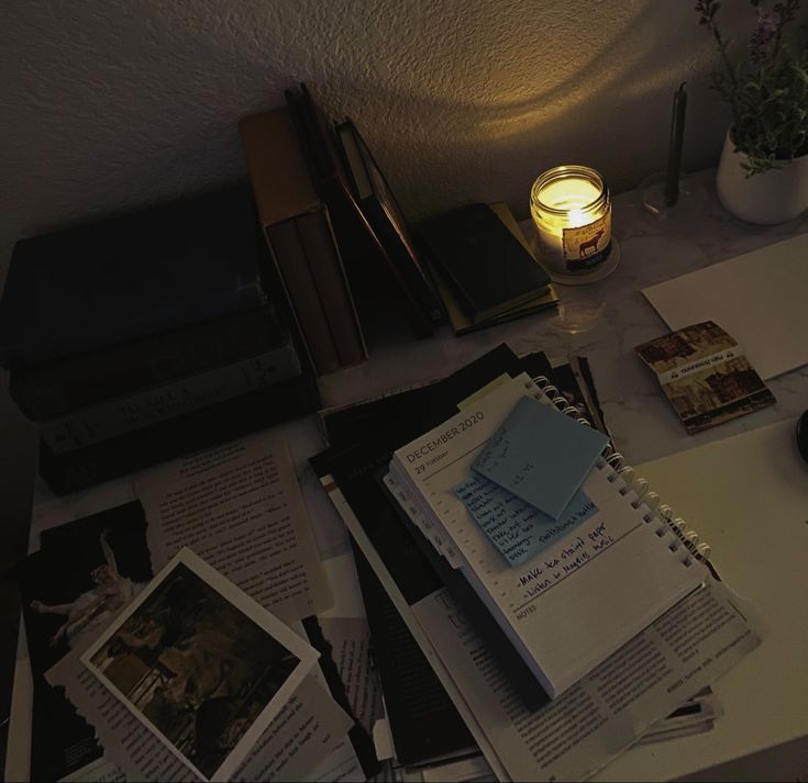 a table topped with books and papers next to a lamp on top of a desk