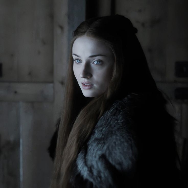 a woman with long hair and blue eyes standing in a dark room, looking at the camera