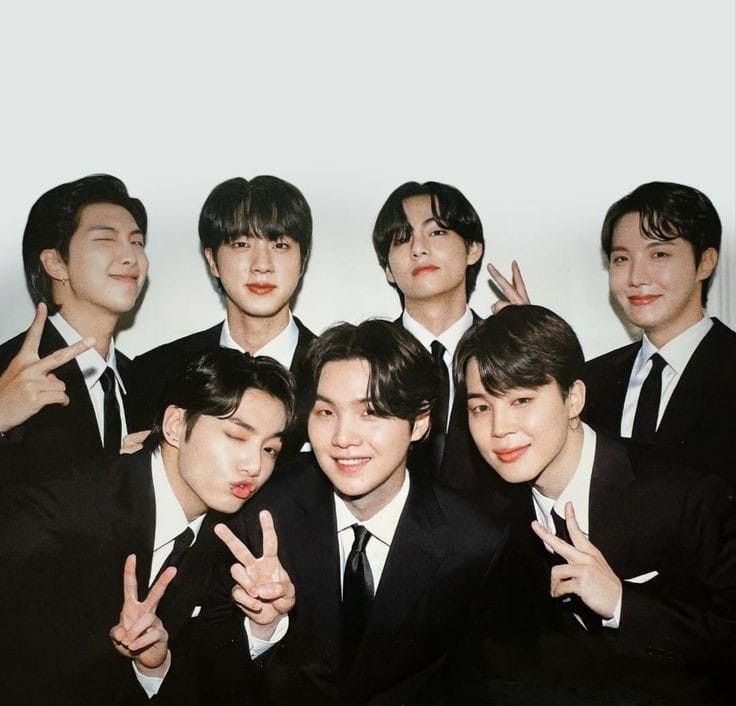 a group of young men in suits posing for the camera with their fingers up and one hand making the peace sign