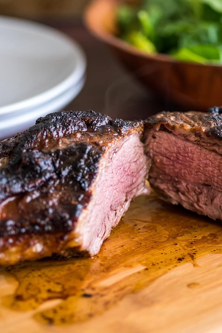 a piece of meat on a wooden cutting board next to a bowl of lettuce