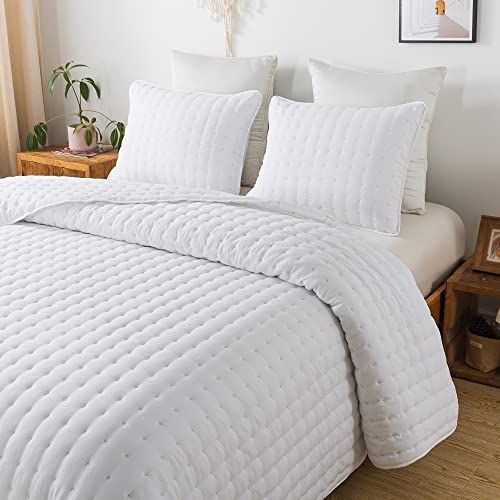 a bed with white comforter and pillows in a room next to a wooden table