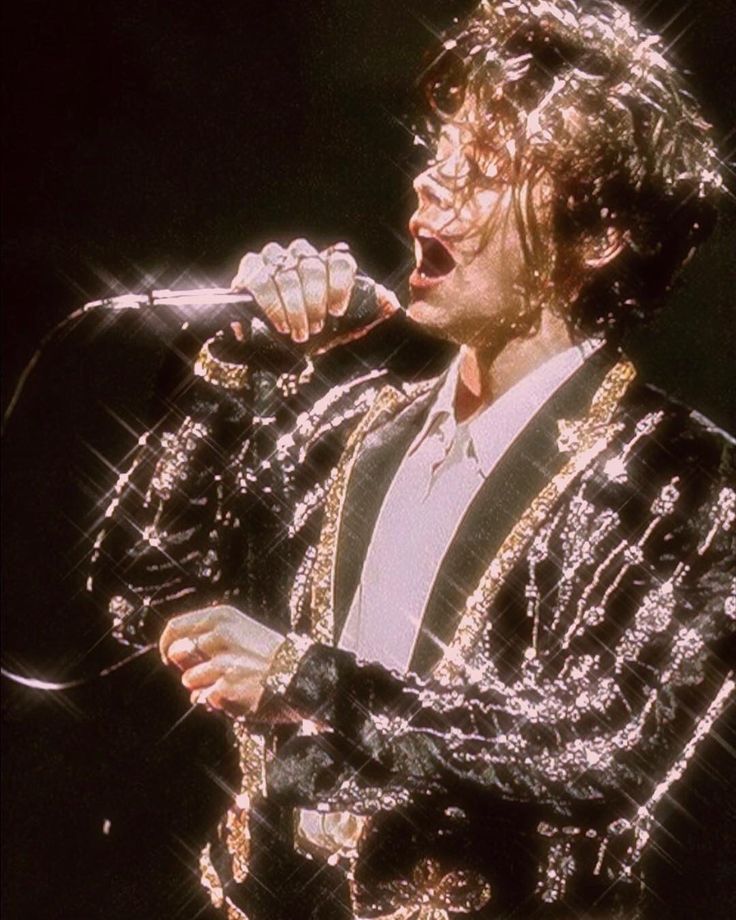 the singer is singing into his microphone while wearing a suit and holding a microphone in his right hand