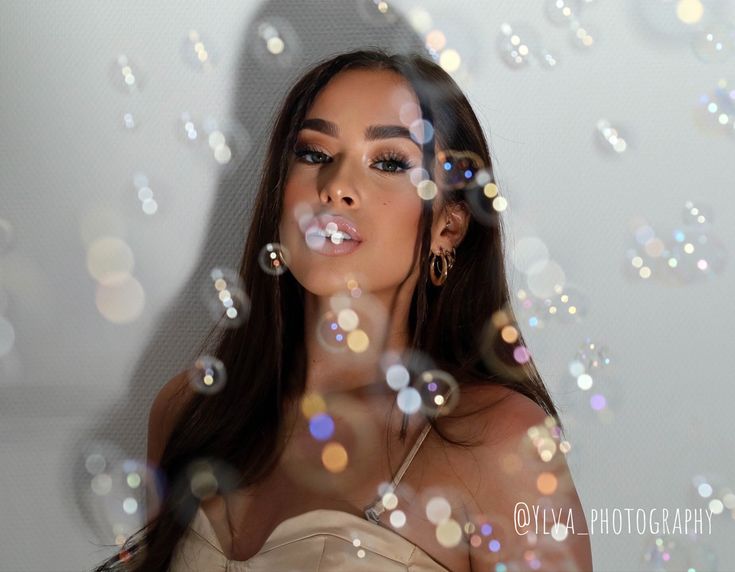 a woman with long hair blowing bubbles in front of her face and looking at the camera