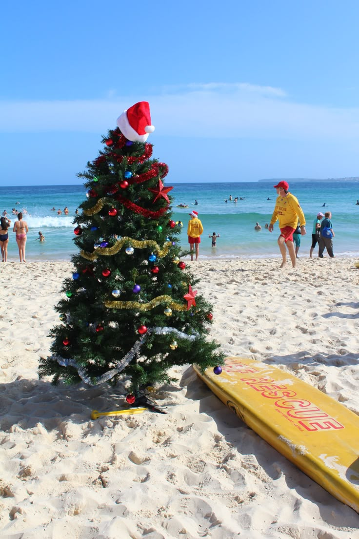 a christmas tree on the beach with people in the water and one surfboard under it