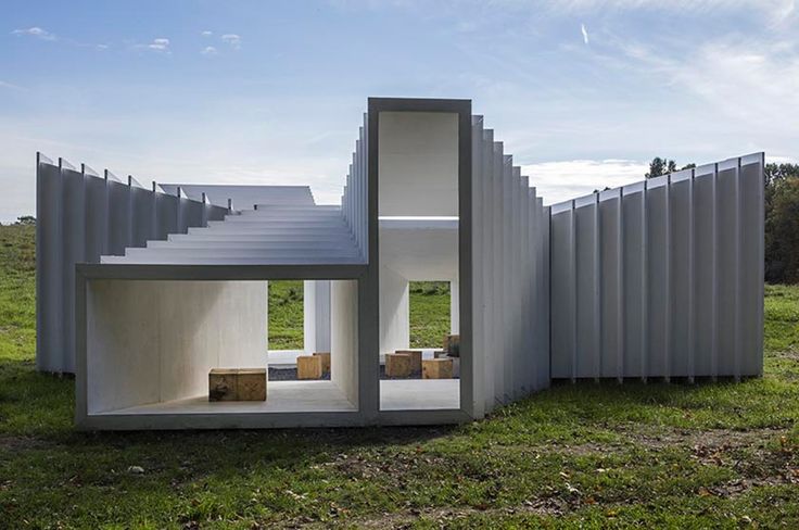 a house made out of white corrugated sheets on top of a grass covered field with trees in the background