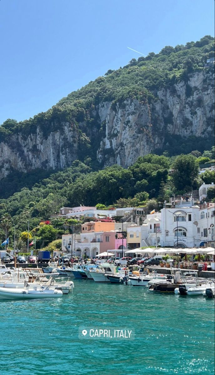 several boats are docked in the water near some mountains and houses on top of a hill