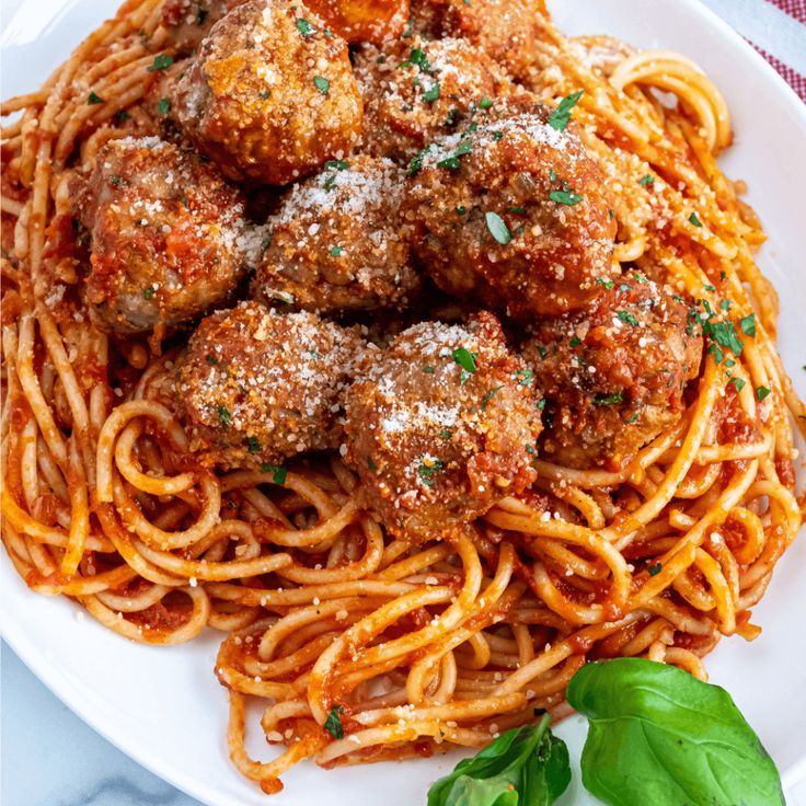 spaghetti with meatballs and tomato sauce on a white plate, garnished with fresh basil