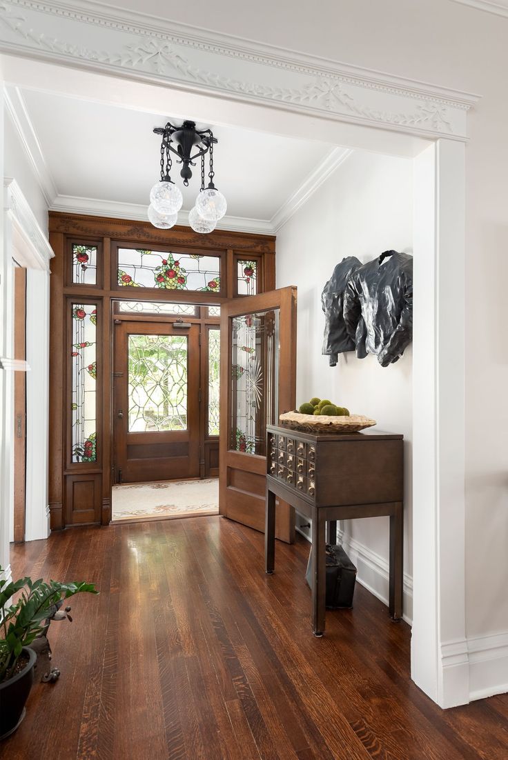 an entryway with wood floors and white walls, two plants on the end table