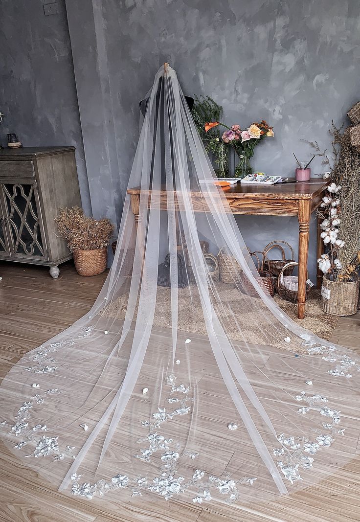 a wedding veil with white flowers on the floor in front of a table and chair