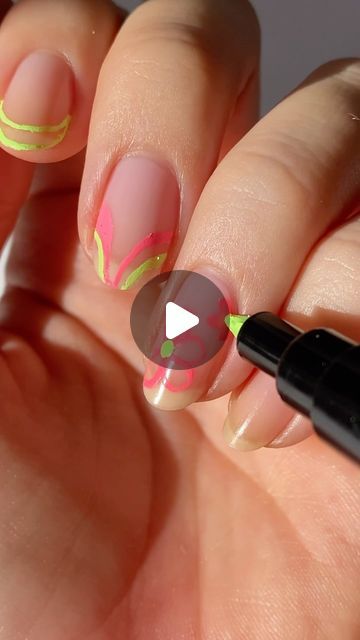 a woman's hand with pink and yellow nail designs on it, holding a black marker