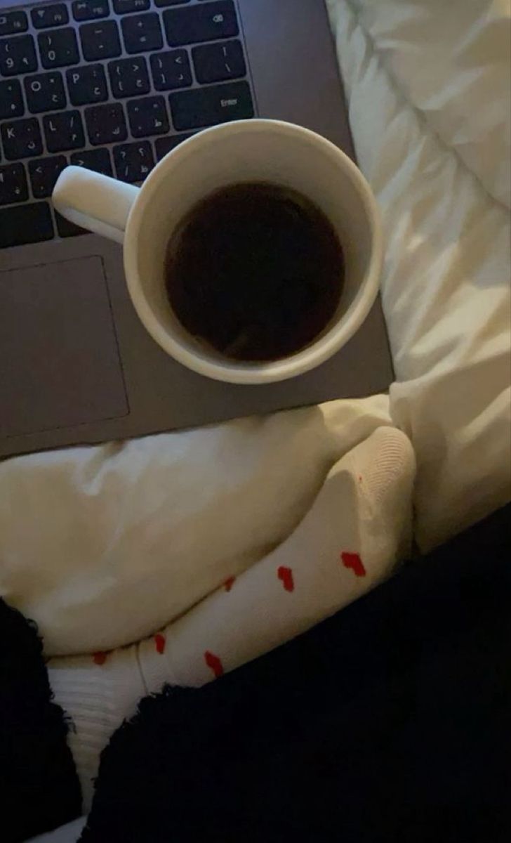 a cup of coffee sitting on top of a bed next to a laptop computer