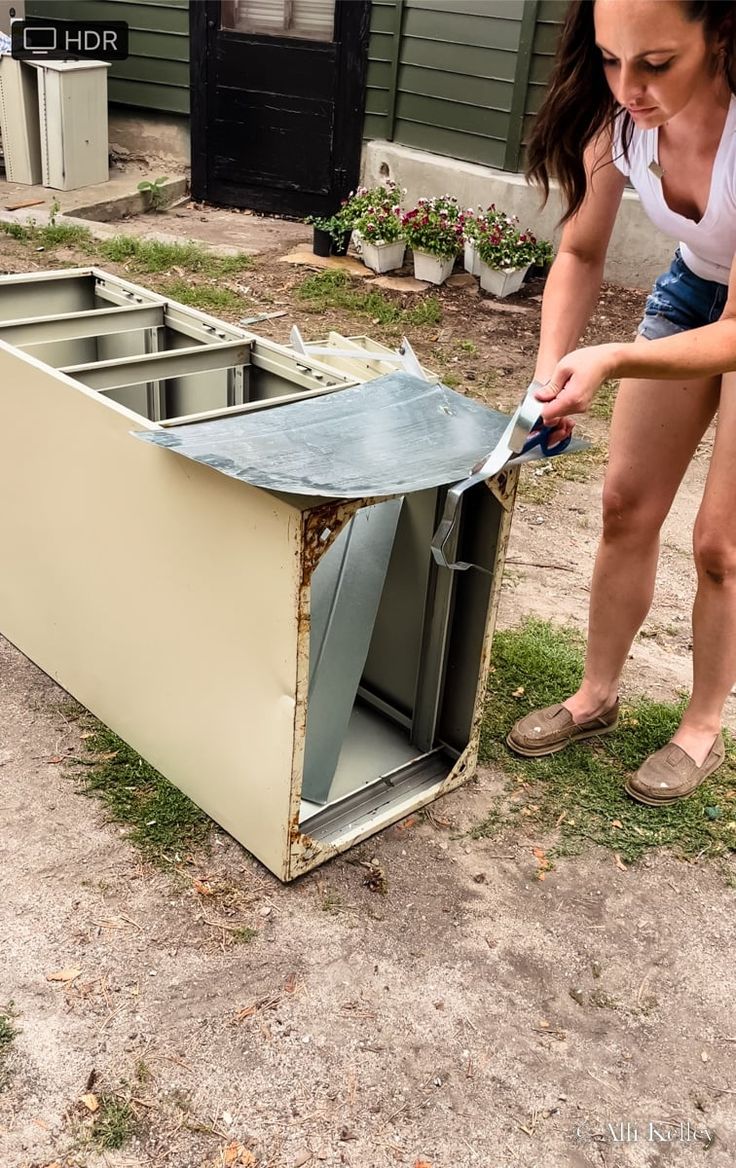 a woman is bending over to put something in an old box on the ground outside