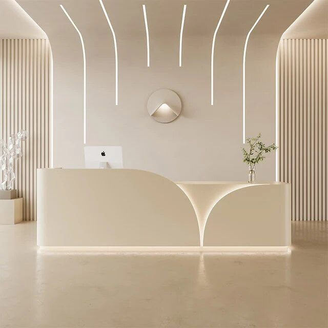 a white reception desk in an empty room with lights on the ceiling and a circular mirror above it