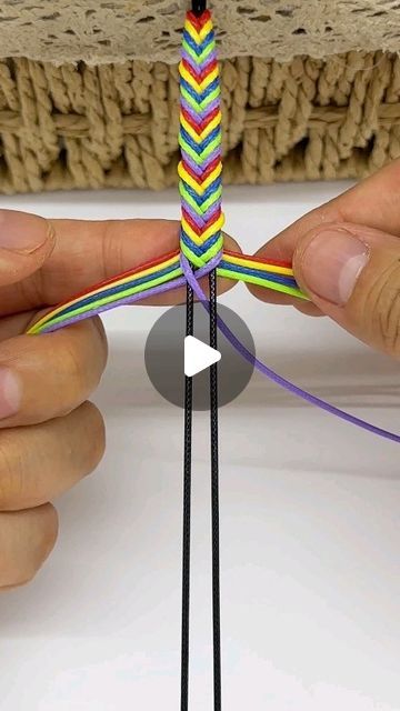 two hands are working on a multicolored string