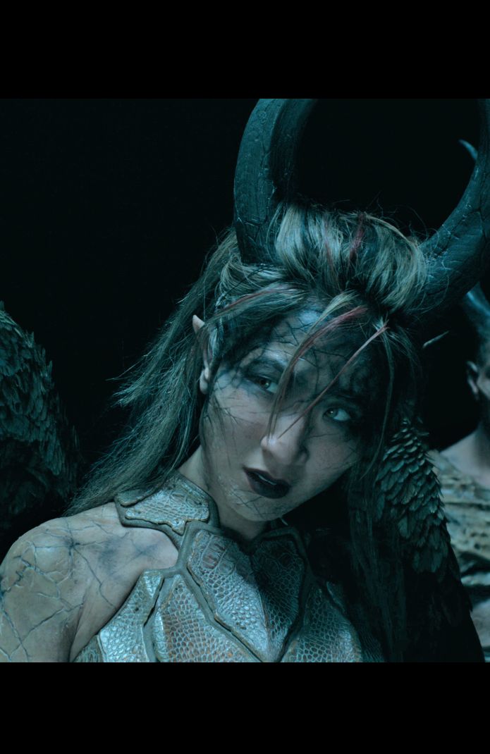 a woman with long hair and horns standing in front of two other women wearing horned headdresses