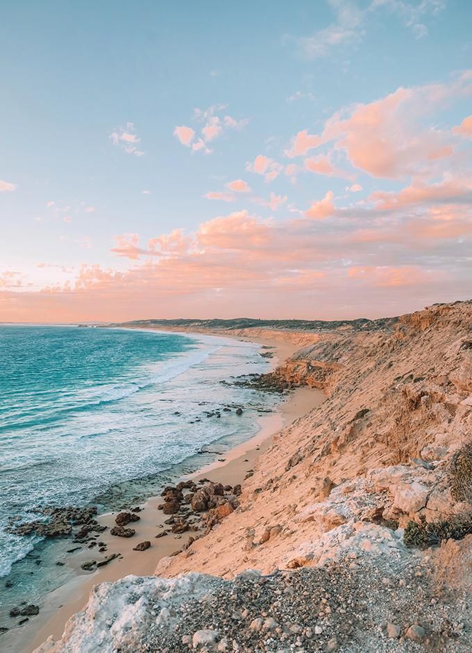 the beach is covered with rocks and sand as the sun sets over the water in the distance