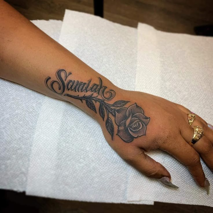 a woman's hand with a rose tattoo on it and the word sandal written in cursive font