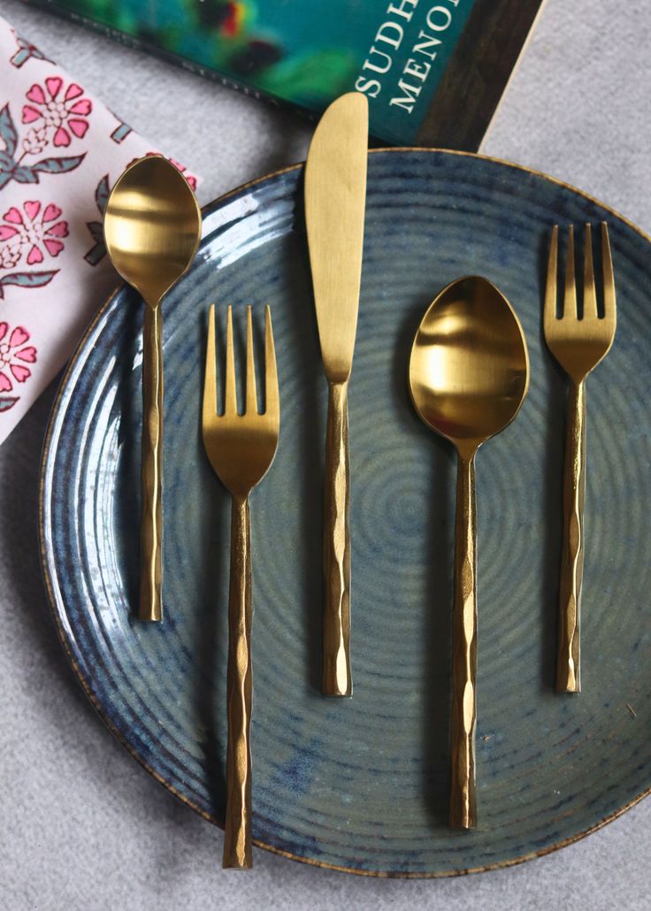 three forks and two spoons on a blue plate with a book in the background