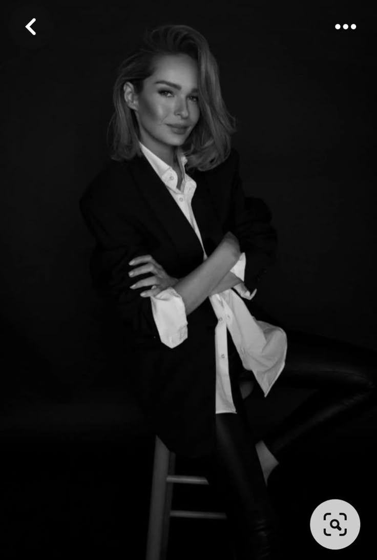 a woman posing for a black and white photo with her arms crossed, leaning on a bar stool